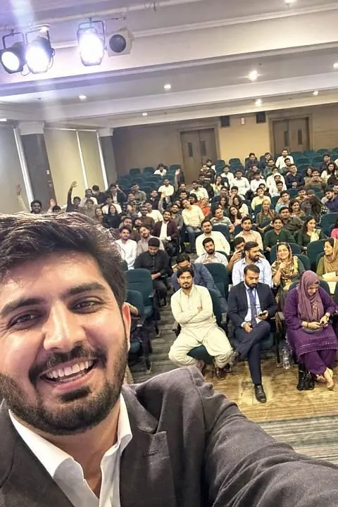 Hassaan Bukhari taking a selfie from the stage with a seminar audience behind him