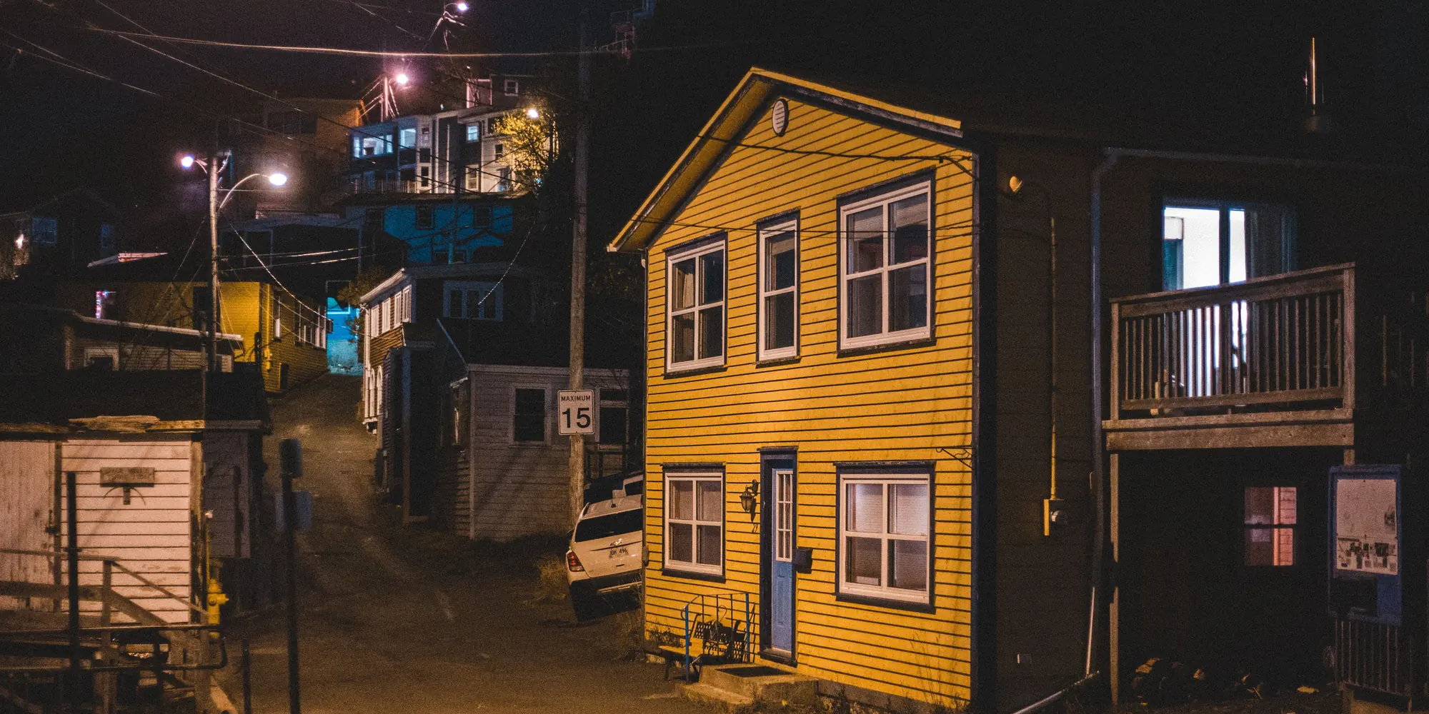 A suburban street at night with lit windows in the houses