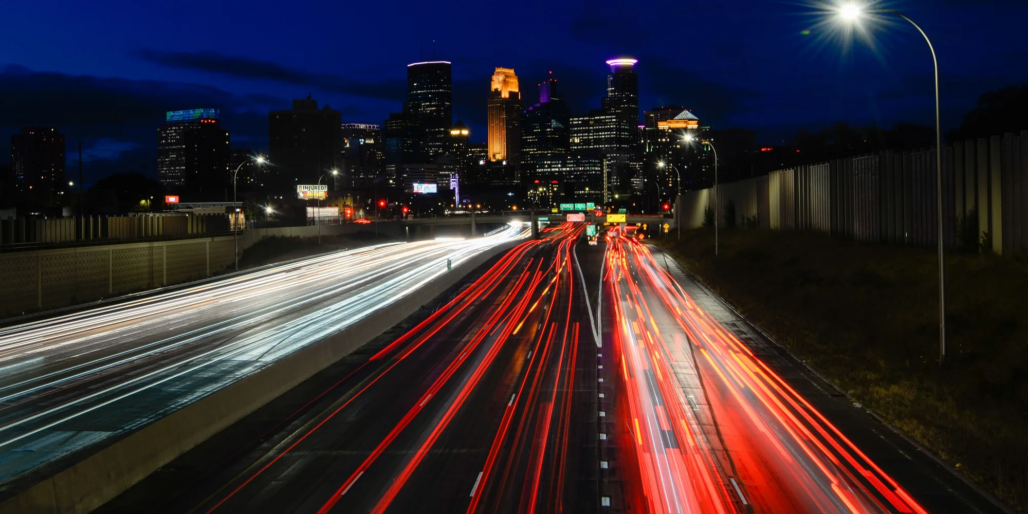 A city skyline at night with car light trails running toward it