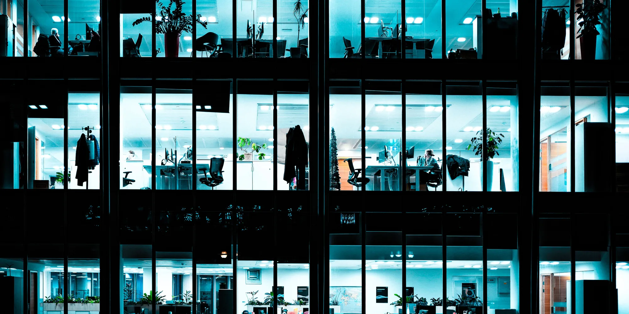 An office building at night, its windows lit and the desks still occupied