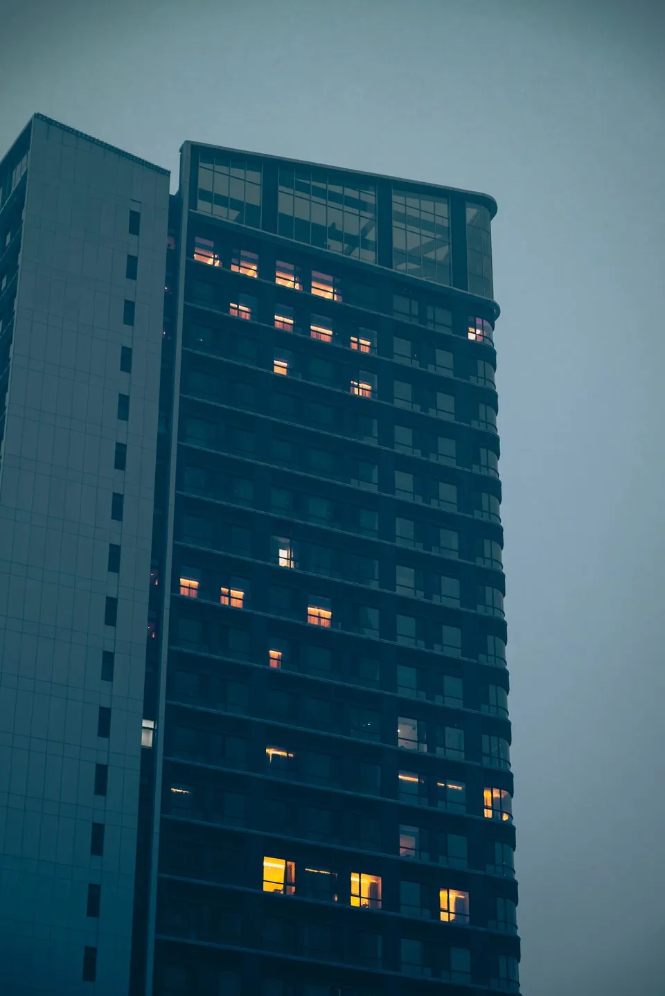 A modern office tower at dusk, seen from below, with lit windows