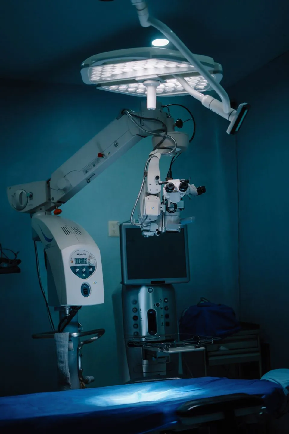 A surgical microscope and monitor in a treatment room lit in teal