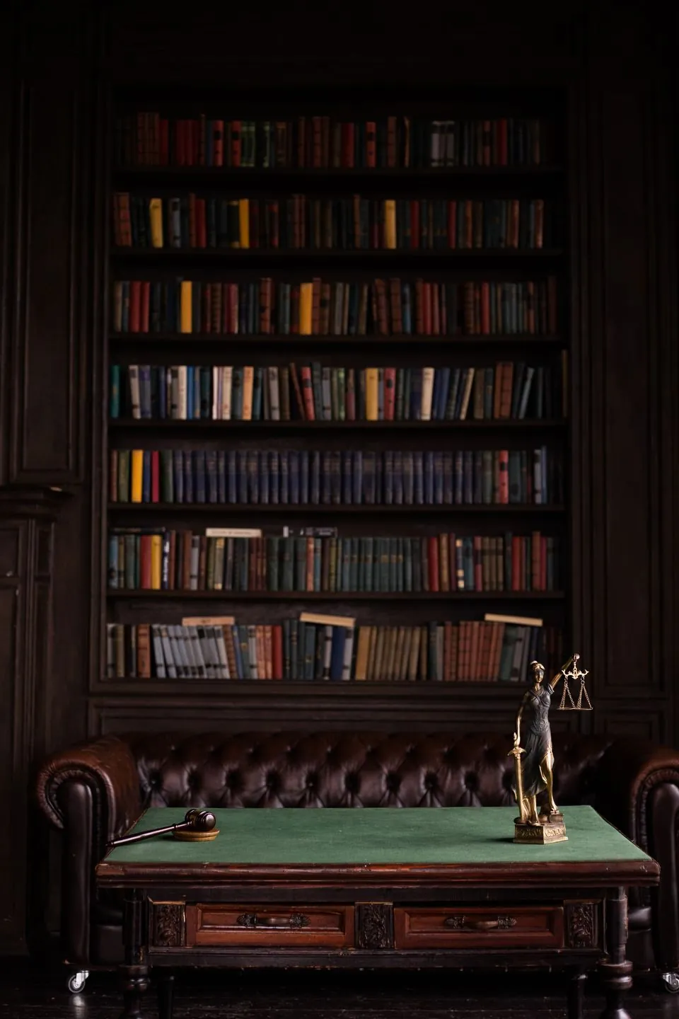 A law library shelf behind a desk with a small figure of justice and a gavel